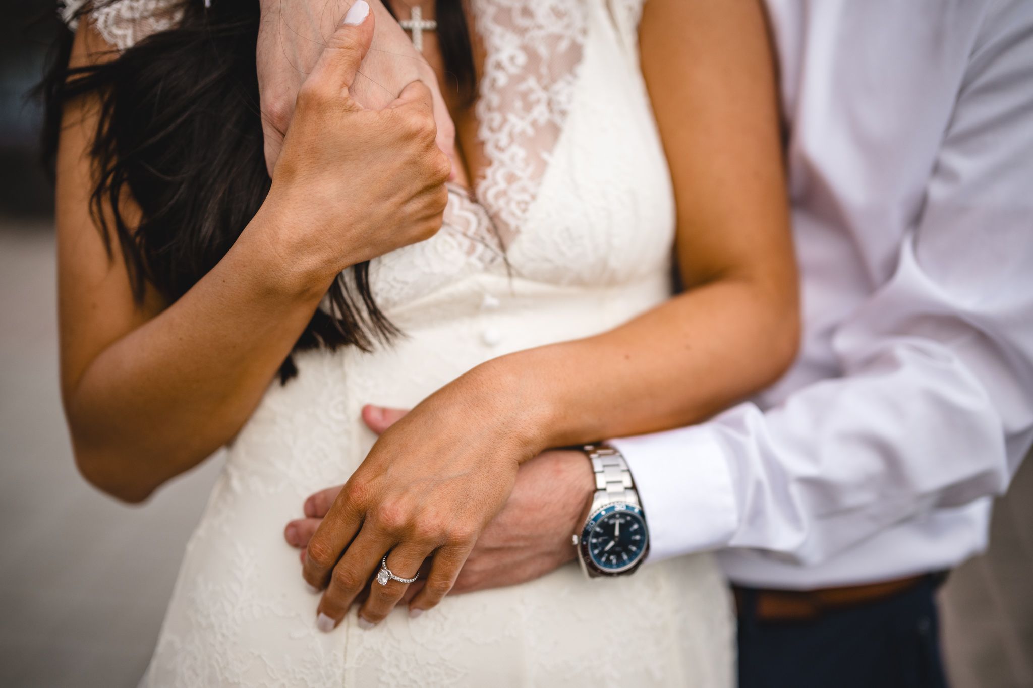 Close-up of bride and groom embracing, showing wedding rings and watch details.