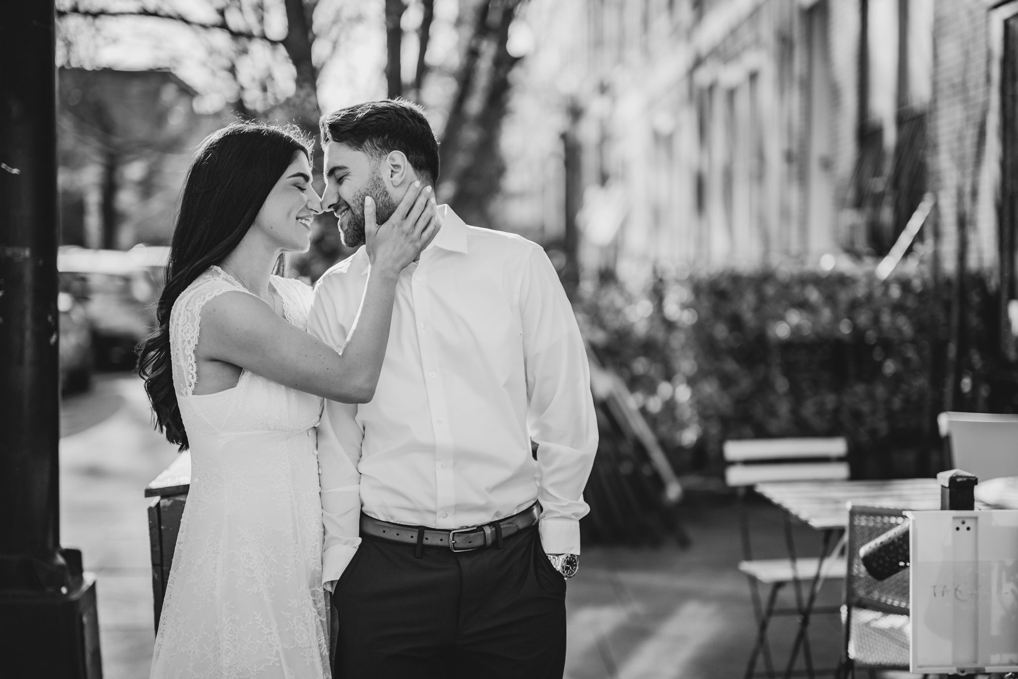 Black and white photo of a romantic couple sharing an intimate moment on a city street, woman touching mans face.
