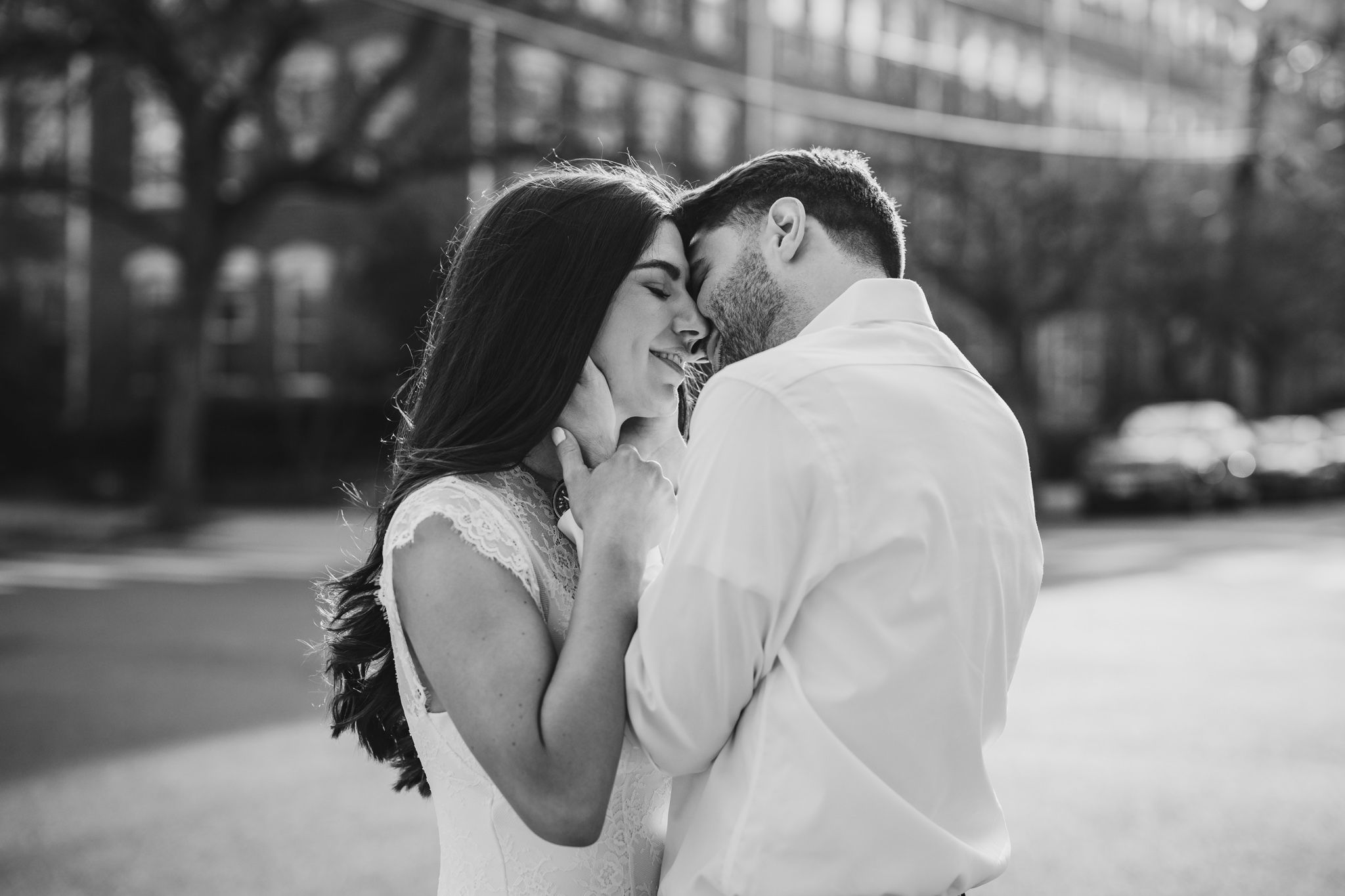 Black and white romantic couple almost kissing outdoors with soft bokeh city background.