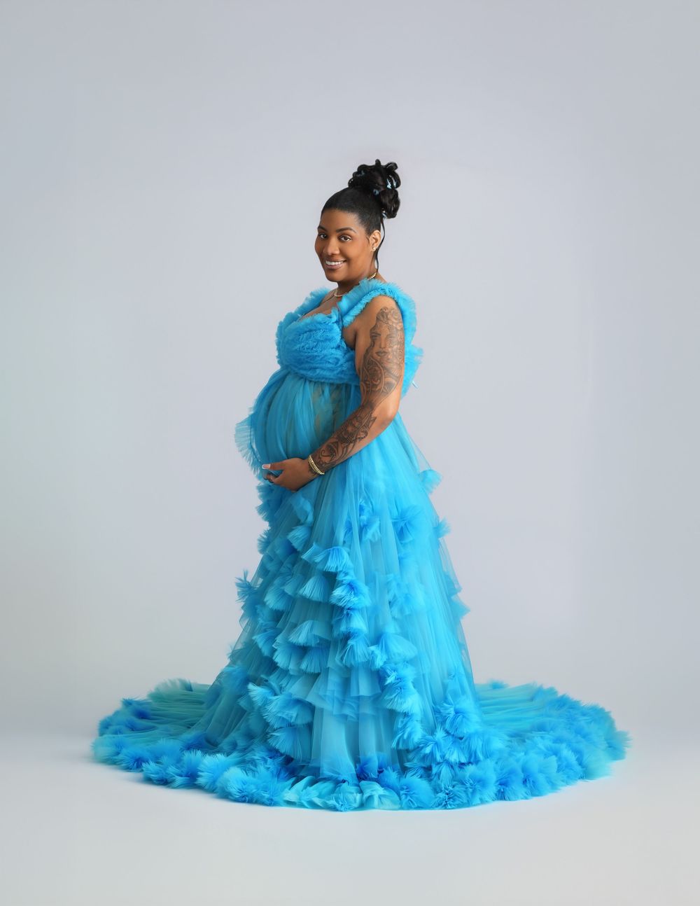 Pregnant woman in a stunning blue ruffled tulle maternity gown posing gracefully in a professional photo studio.