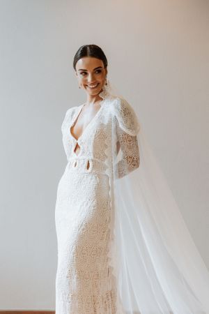 A detailed lace wedding dress with long sleeves and flowing veil photographed against a light background.