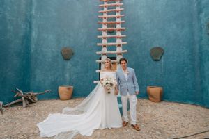 Wedding couple posing against a turquoise wall with their white dog.