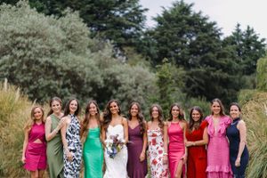 Bridesmaids in colorful dresses ranging from pink to green stand together in an outdoor garden setting.