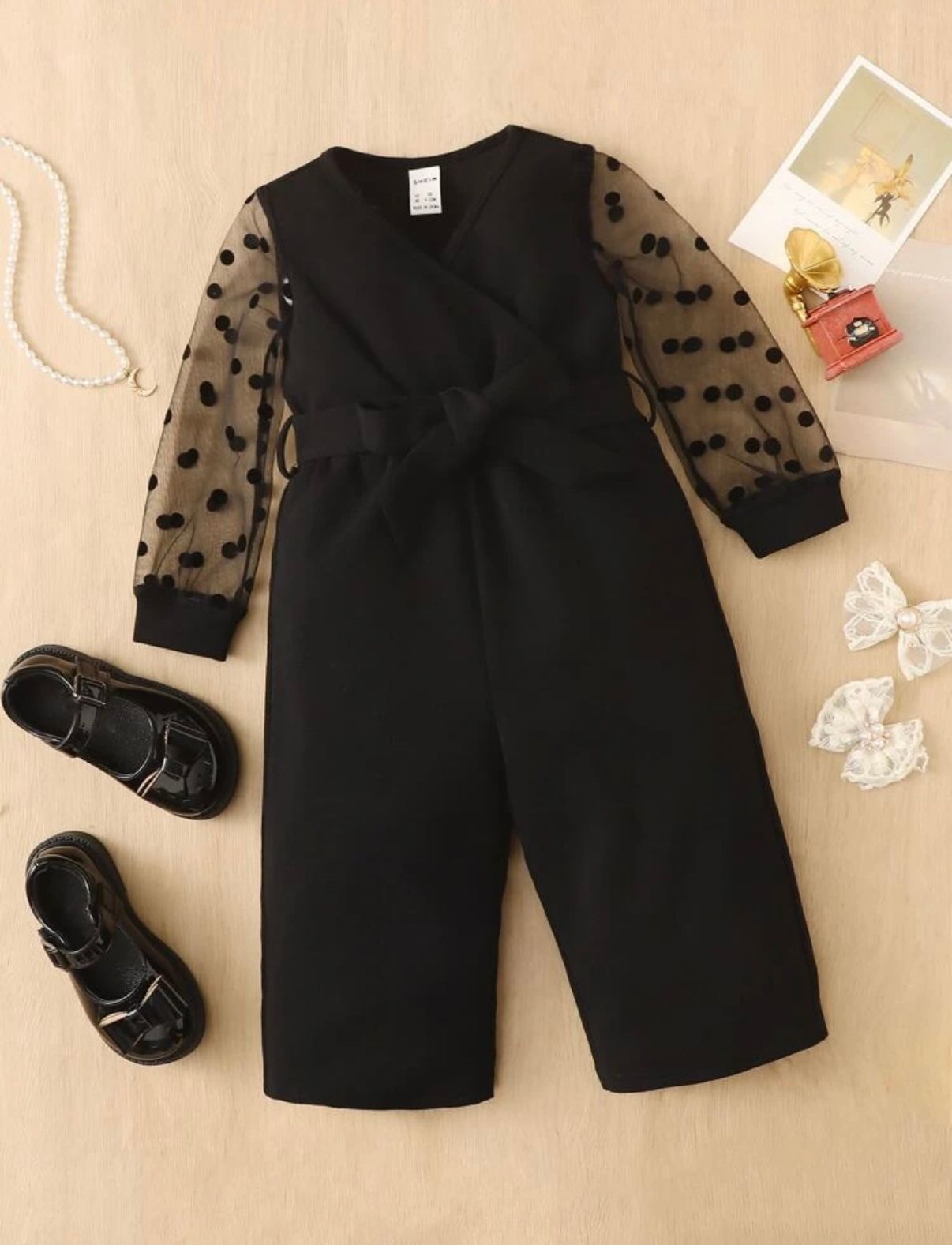 Black formal wear pieces with sheer polka dot sleeves displayed on wooden surface.