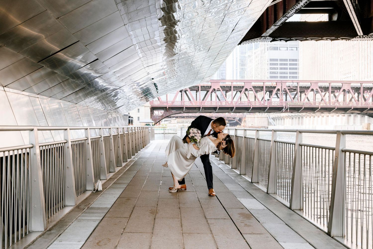 Two people in wedding attire walk up elegant stone stairs of a historic building during a winter day.