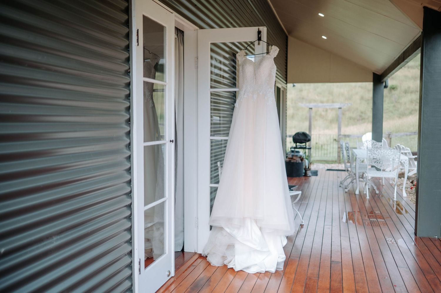 White wedding dress hanging on porch with wooden deck and French doors.