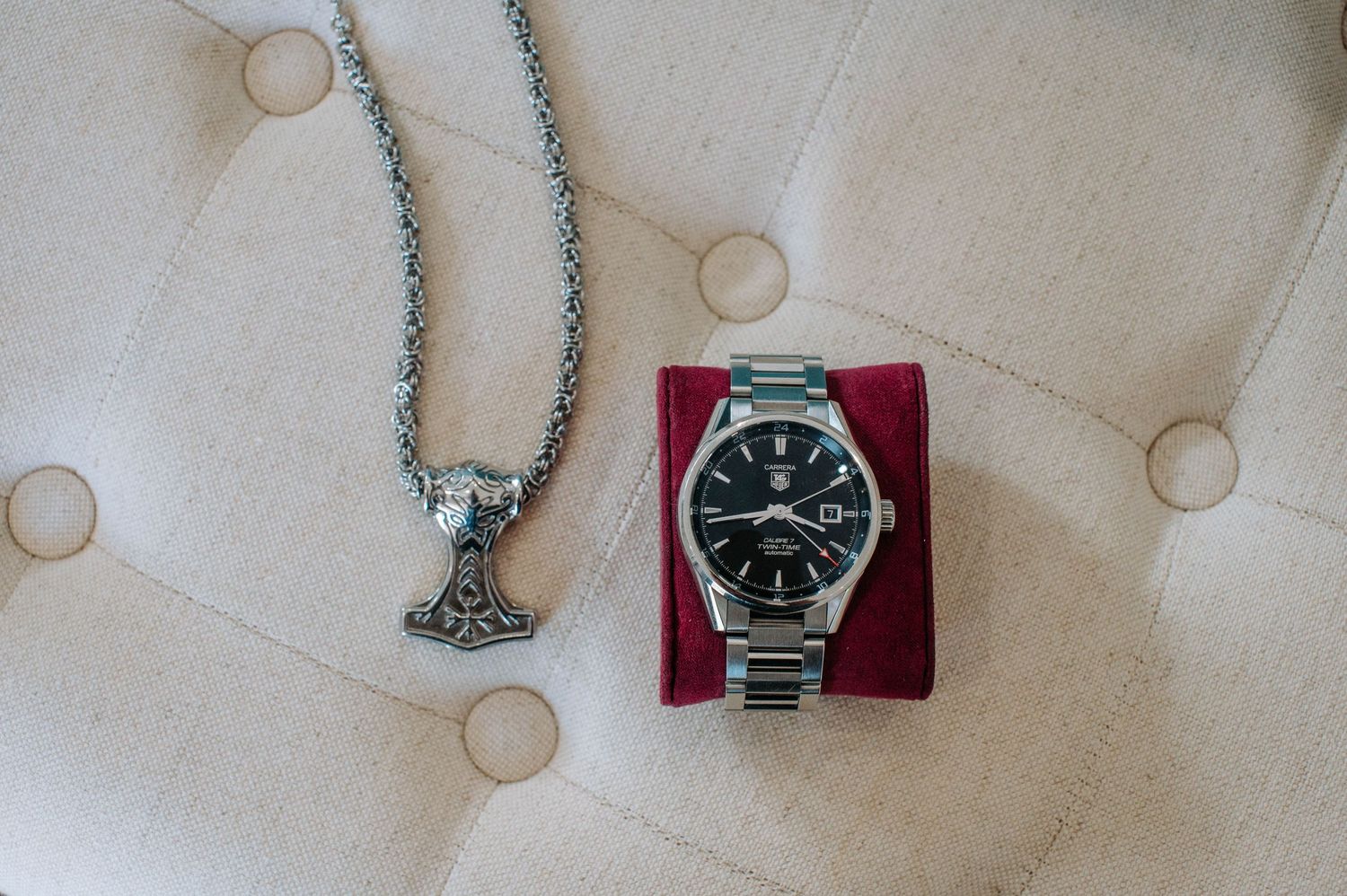 Wedding accessories including silver watch and necklace displayed on white tufted surface.