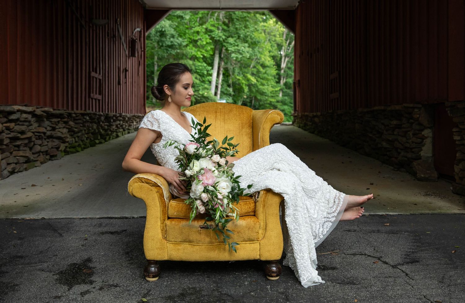 Photo of a bride sitting in a yellow chair in front of a red barn. Elopement photography. Bridal portraits.