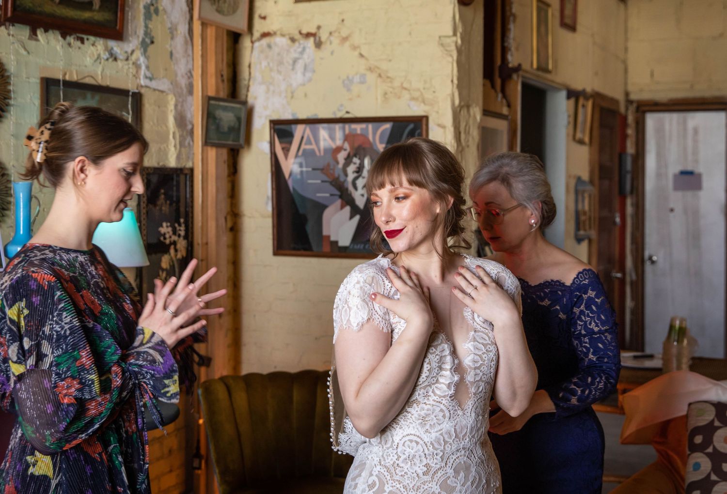 Photo of a bride with her mother and best friend, while her mother adjusts something at the back of the brides dress.