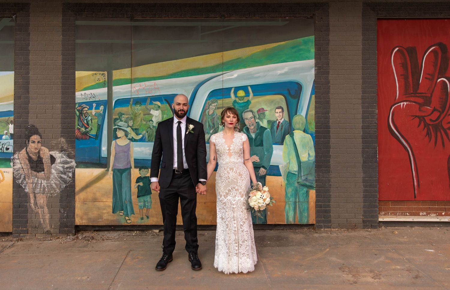 Photo of a bride and groom standing in front of a mural wall, holding hands. Raleigh, NC