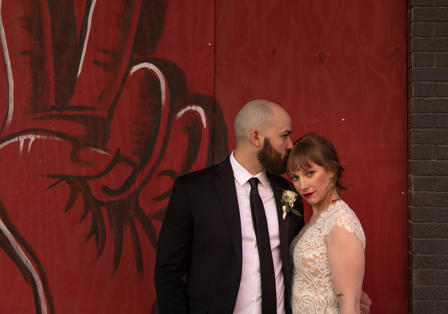 Photo of a bride and groom in front of a red wall with a large hand giving a peace sign on it. Raleigh, NC