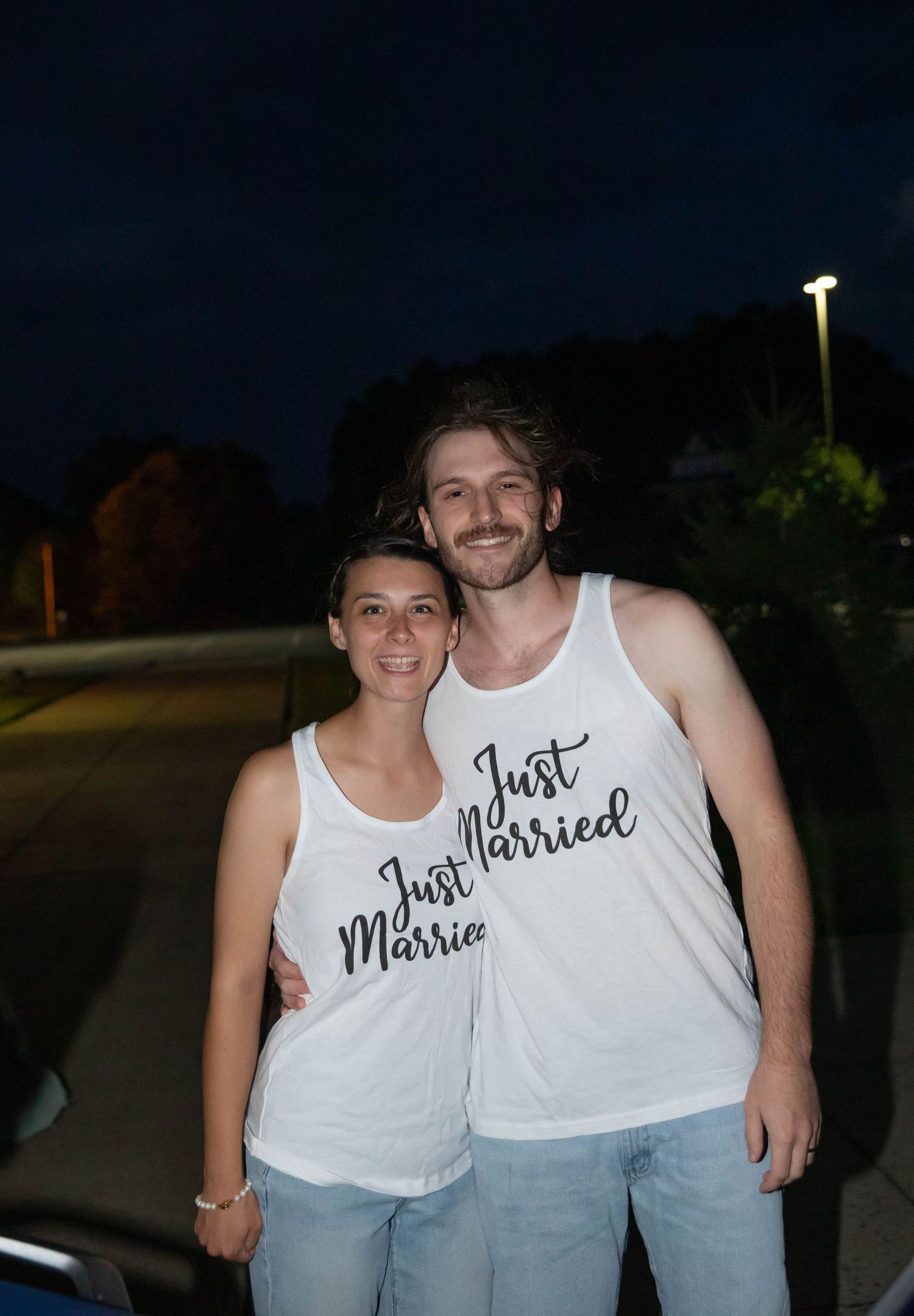 Photo of a bride and groom in white tank tops that say "Just Married" before leaving their reception on a motorcycle. Abingdon, Virginia