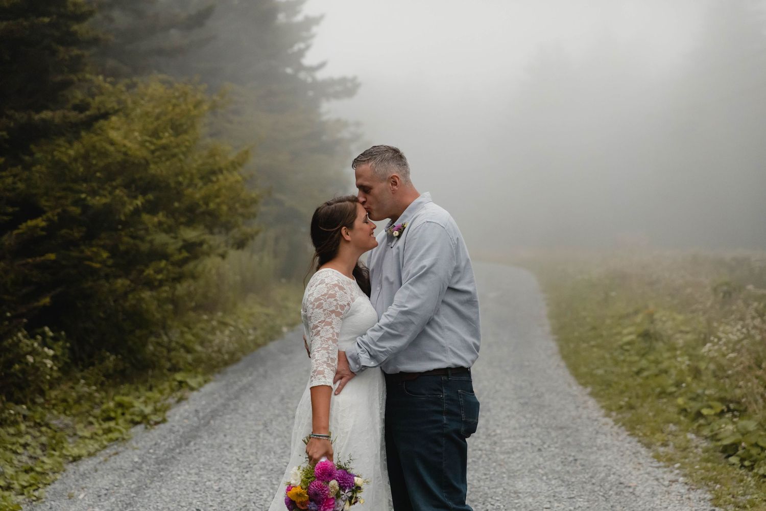 Photo of a bride and groom standing on a gravel road in the woods during a foggy elopement on Whitetop Mountain in southwest Virginia