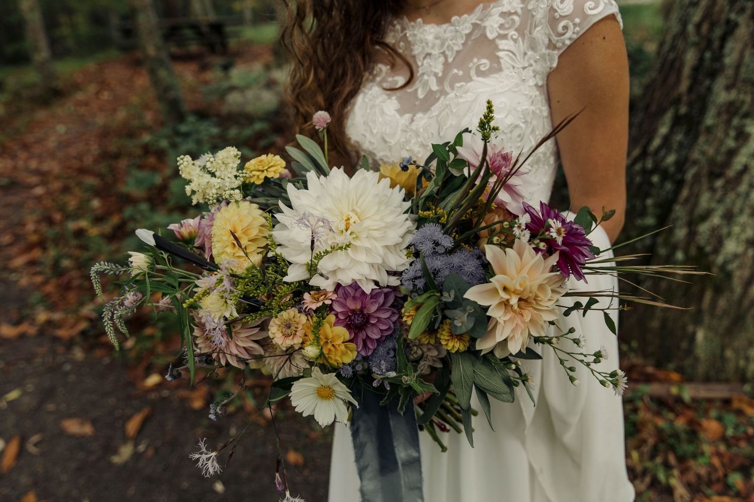 Photo of a bride standing on a trail, holding her wedding bouquet of wildflowers