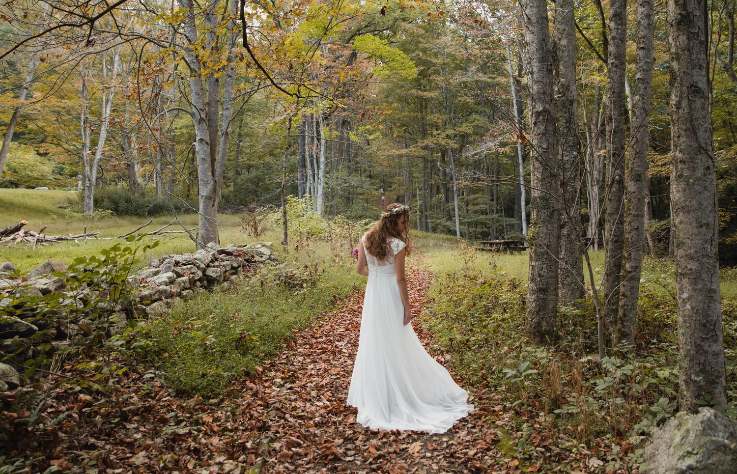 Photo of a bride standing on a trail, looking down at her dress