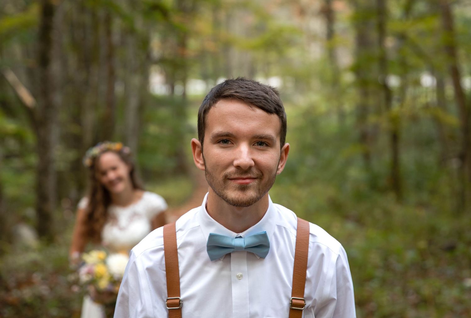 Photo of a bride and groom standing on a trail in the woods, about to do a first look