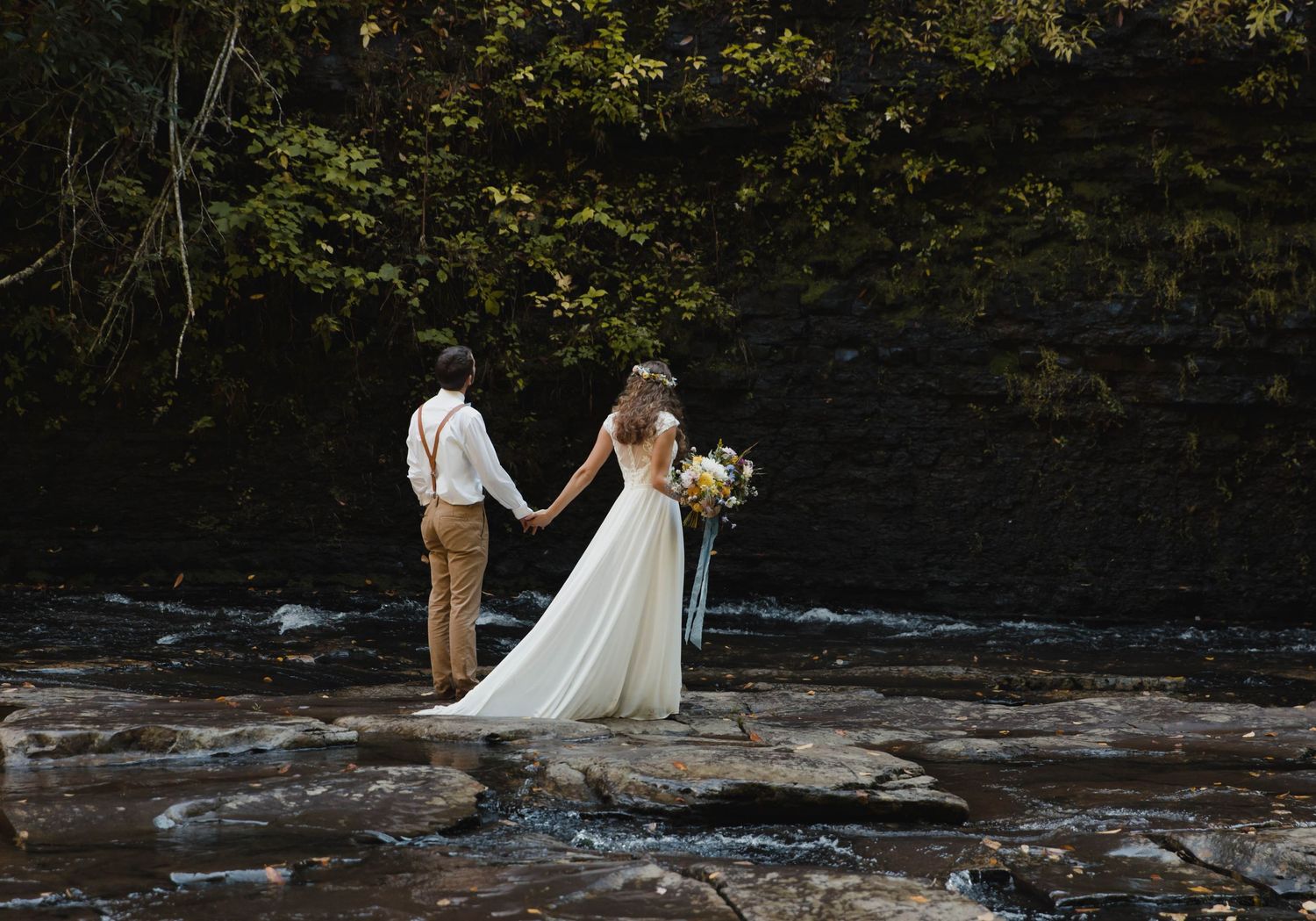 Photo of a bride and groom standing in a creek holding hands at Cascade Falls in Cascades National Recreation Area, Virginia