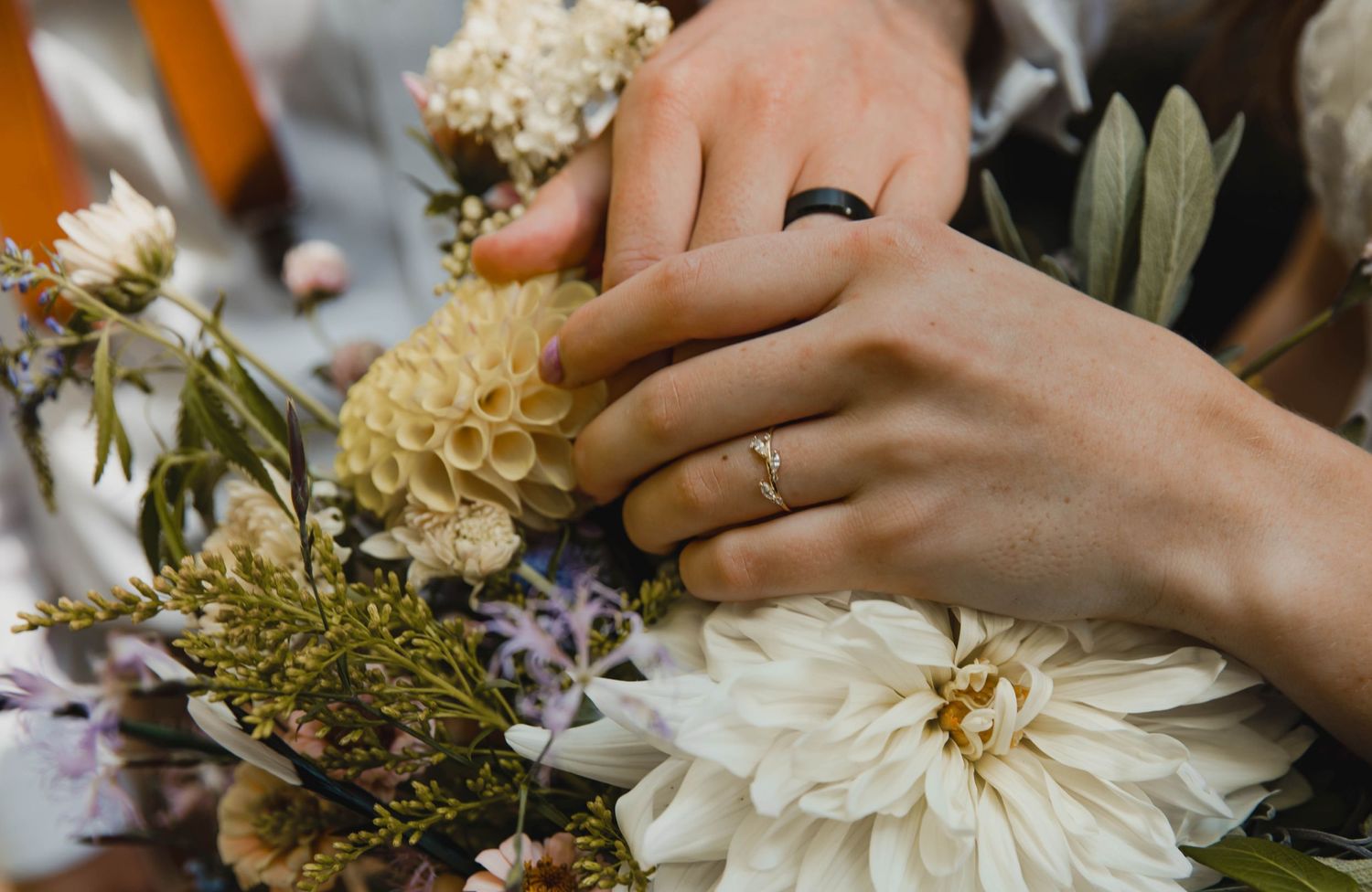 Photos of a bride and grooms hands on top of a bouquet of wildflowers