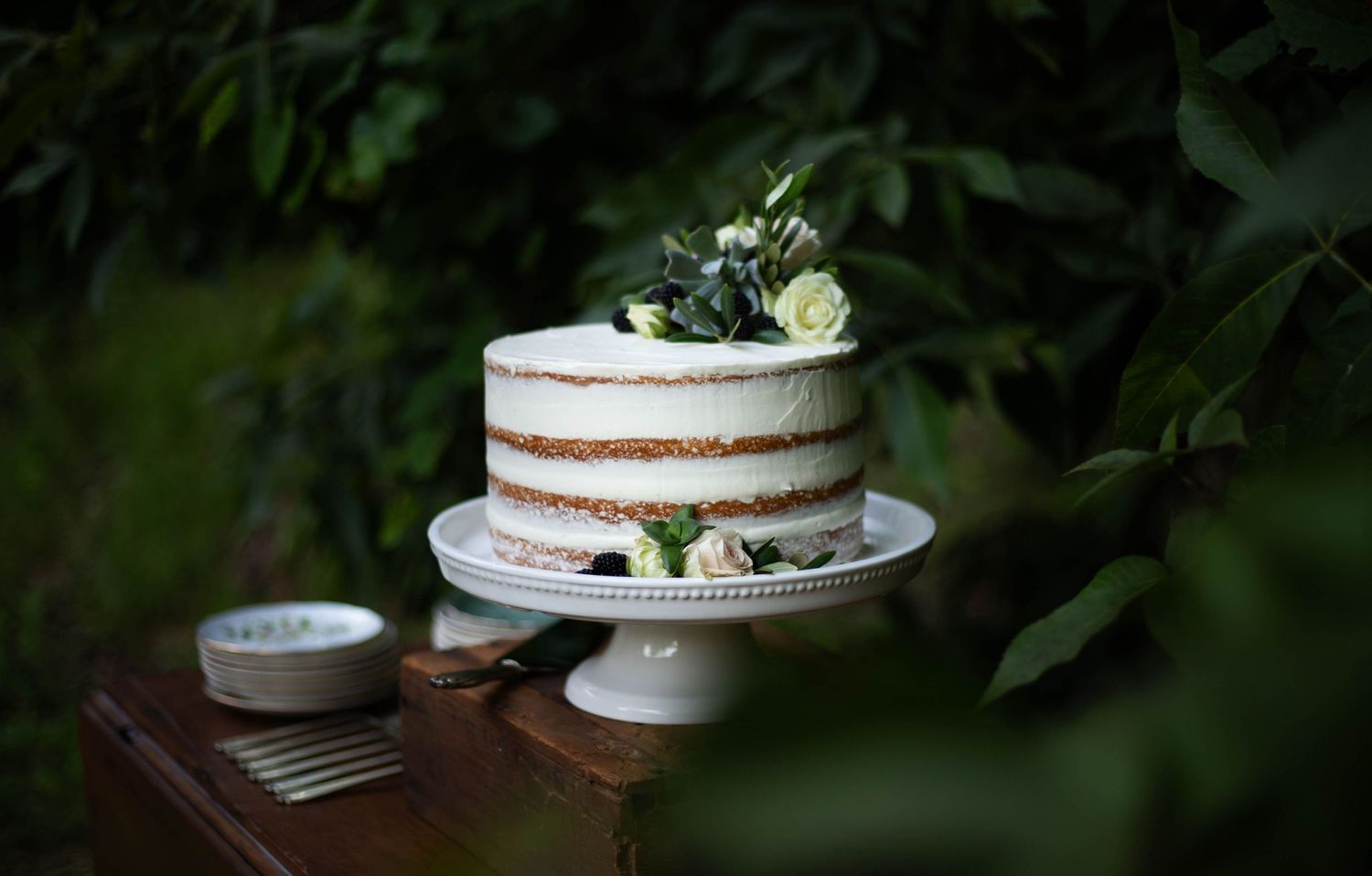 Photo of a wedding cake on a wooden table surrounded by trees