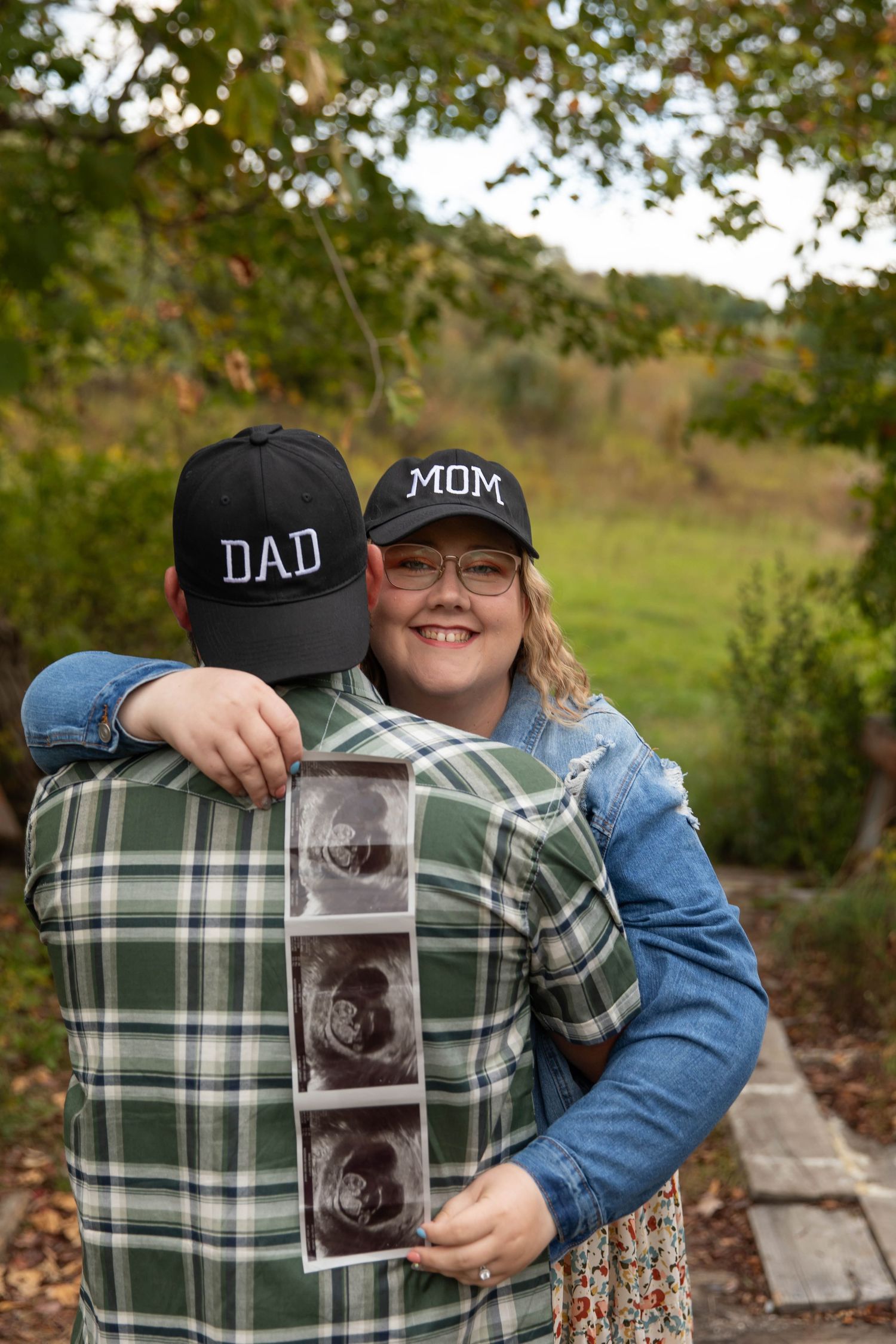 Photo of a couple hugging each other while holding ultrasound photos during a pregnancy announcement photo shoot