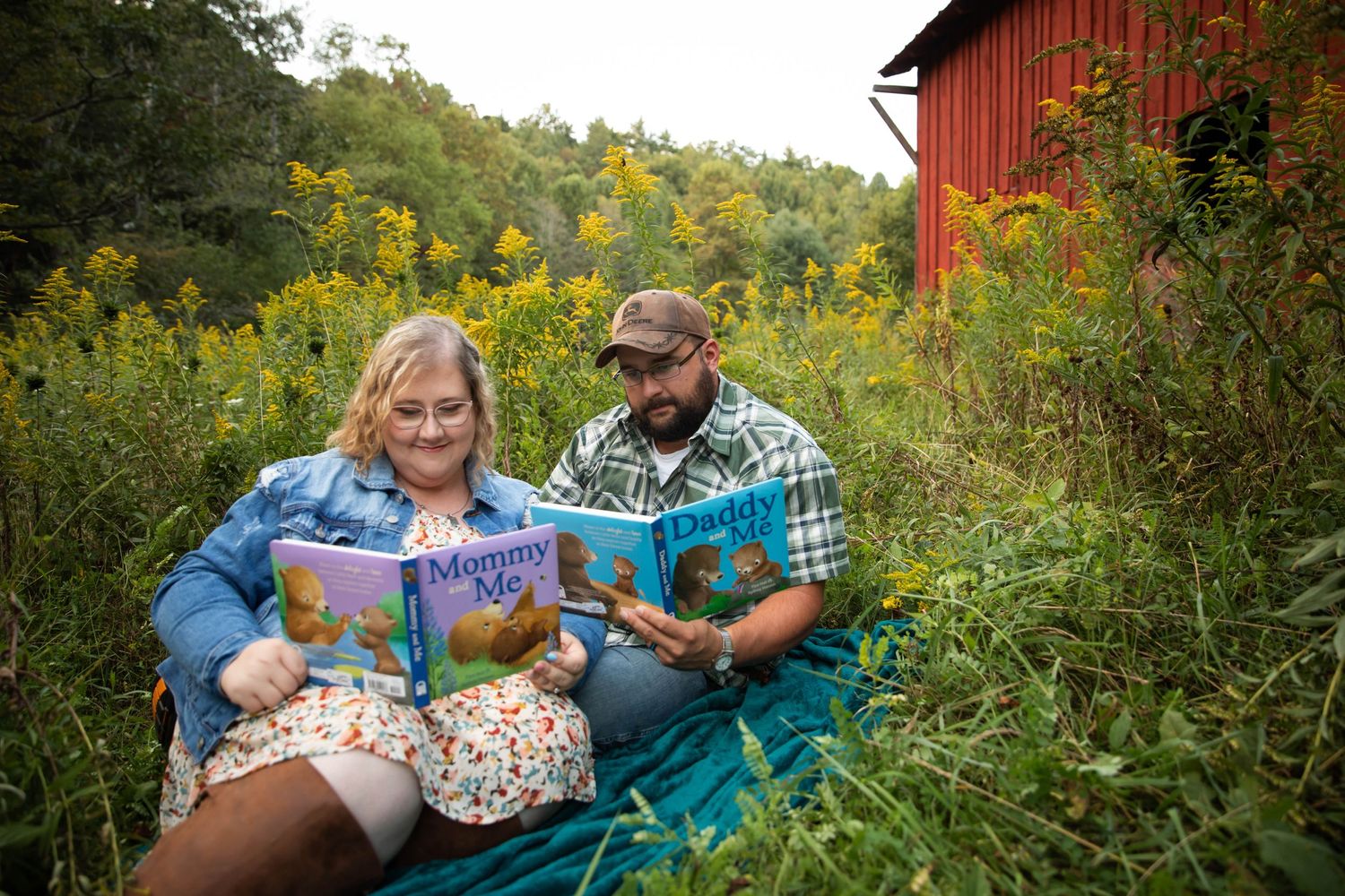 Photo of a couple sitting among yellow flowers in front of a red barn, reading books that say "Mom and Dad" for a pregnancy announcement
