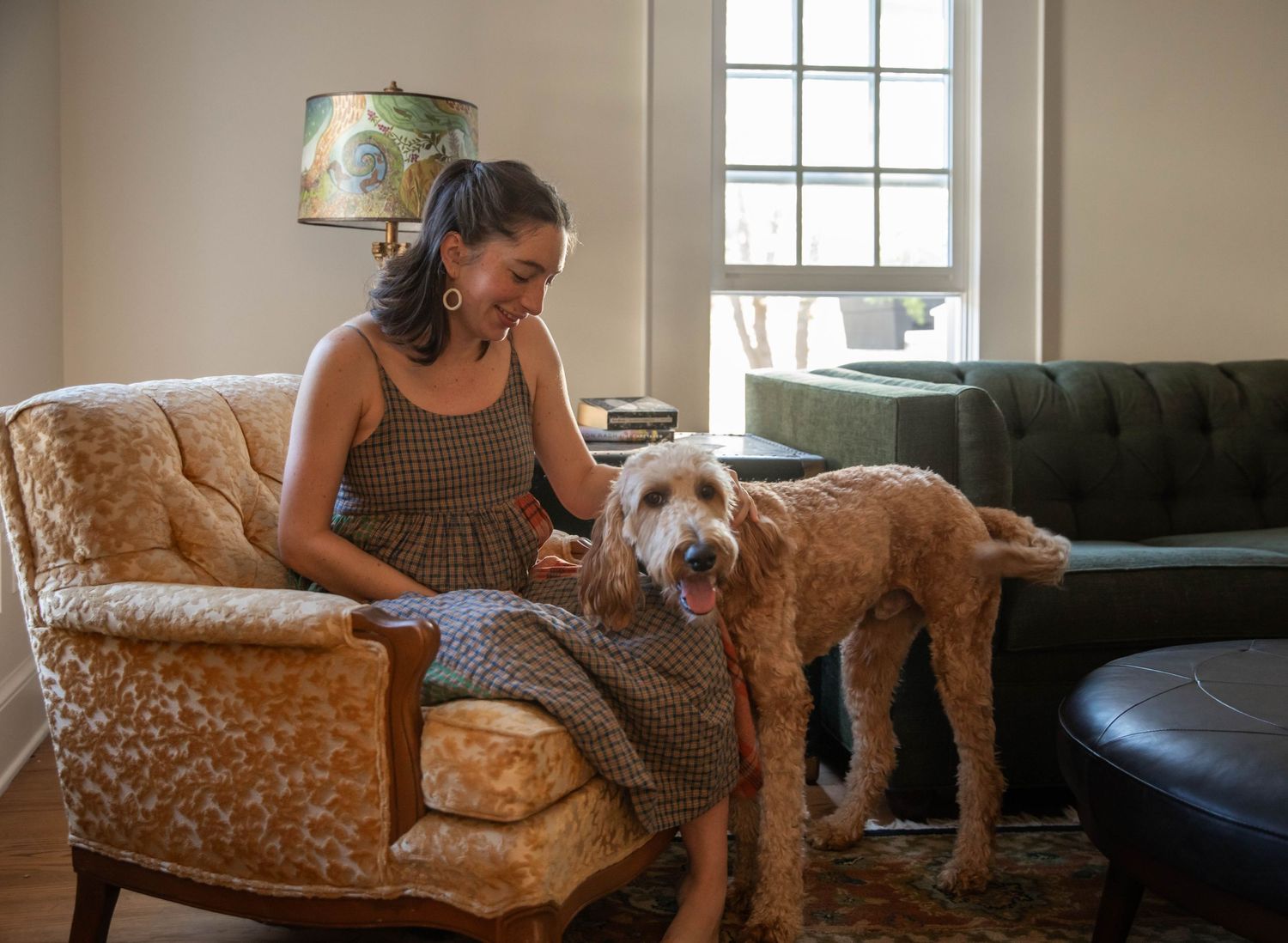 Photo of a pregnant woman sitting in a chair, petting a dog. Taken during a maternity photo shoot