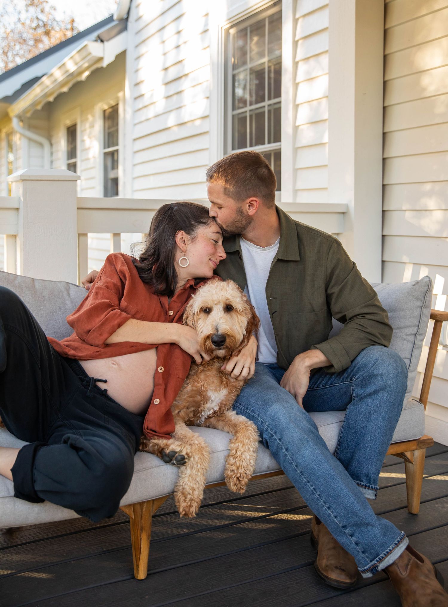 Image of a couple and their dog sitting on the porch, leaning against one another during maternity session