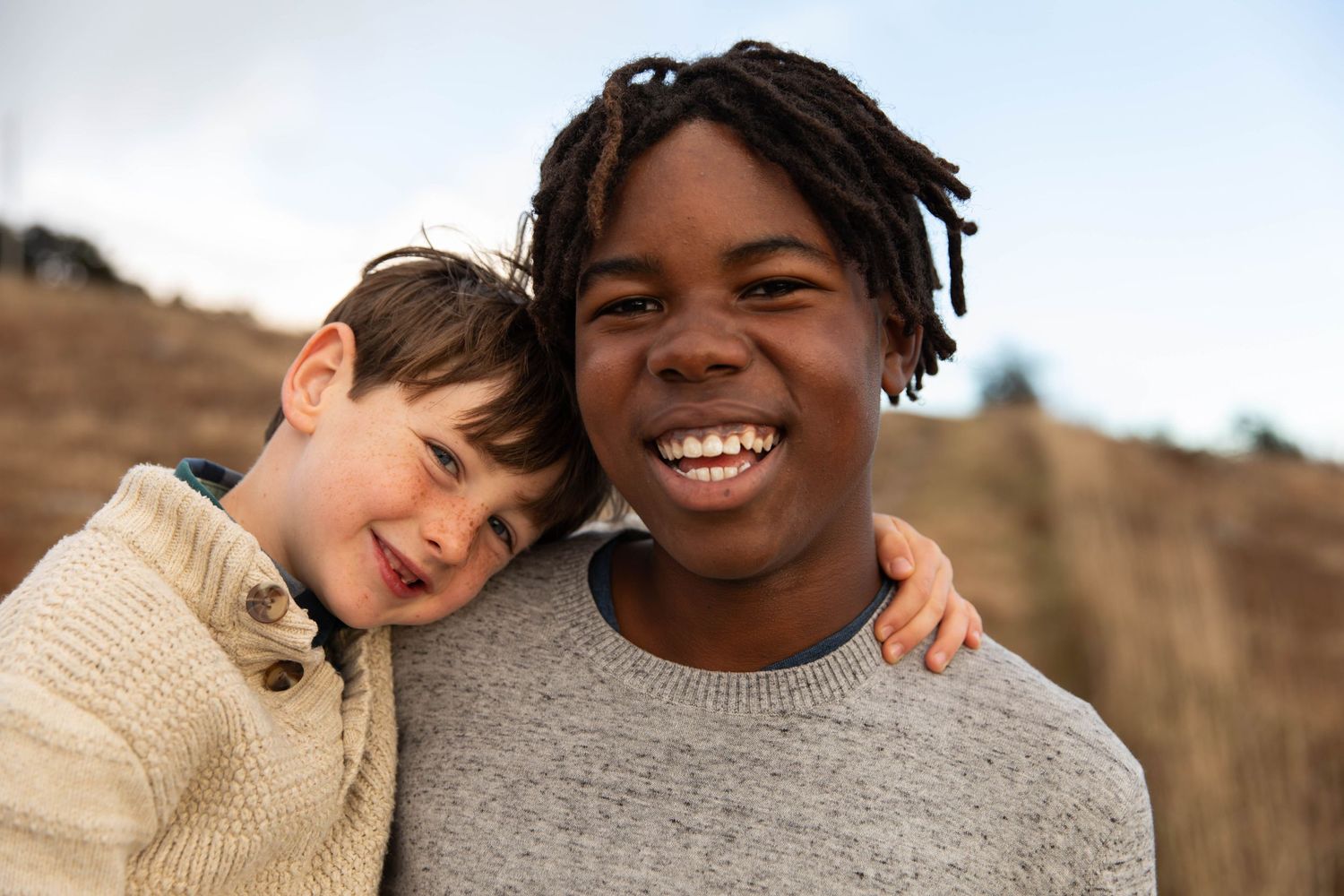 Photo of two brothers smiling at the camera while standing on a mountain during a family photo shoot at sunset
