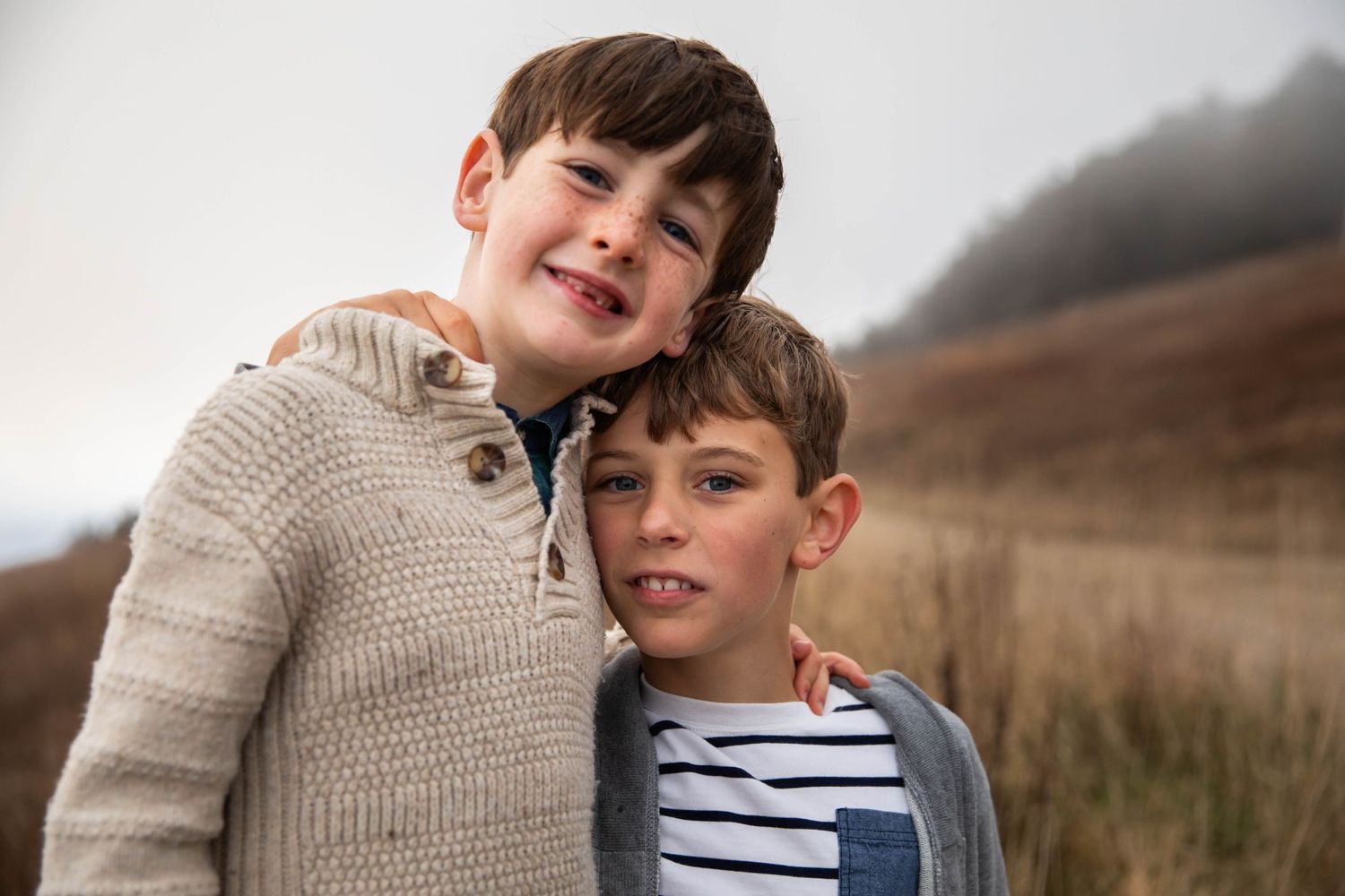 Photo of two brothers smiling at the camera while standing on a foggy mountain during a family photo shoot