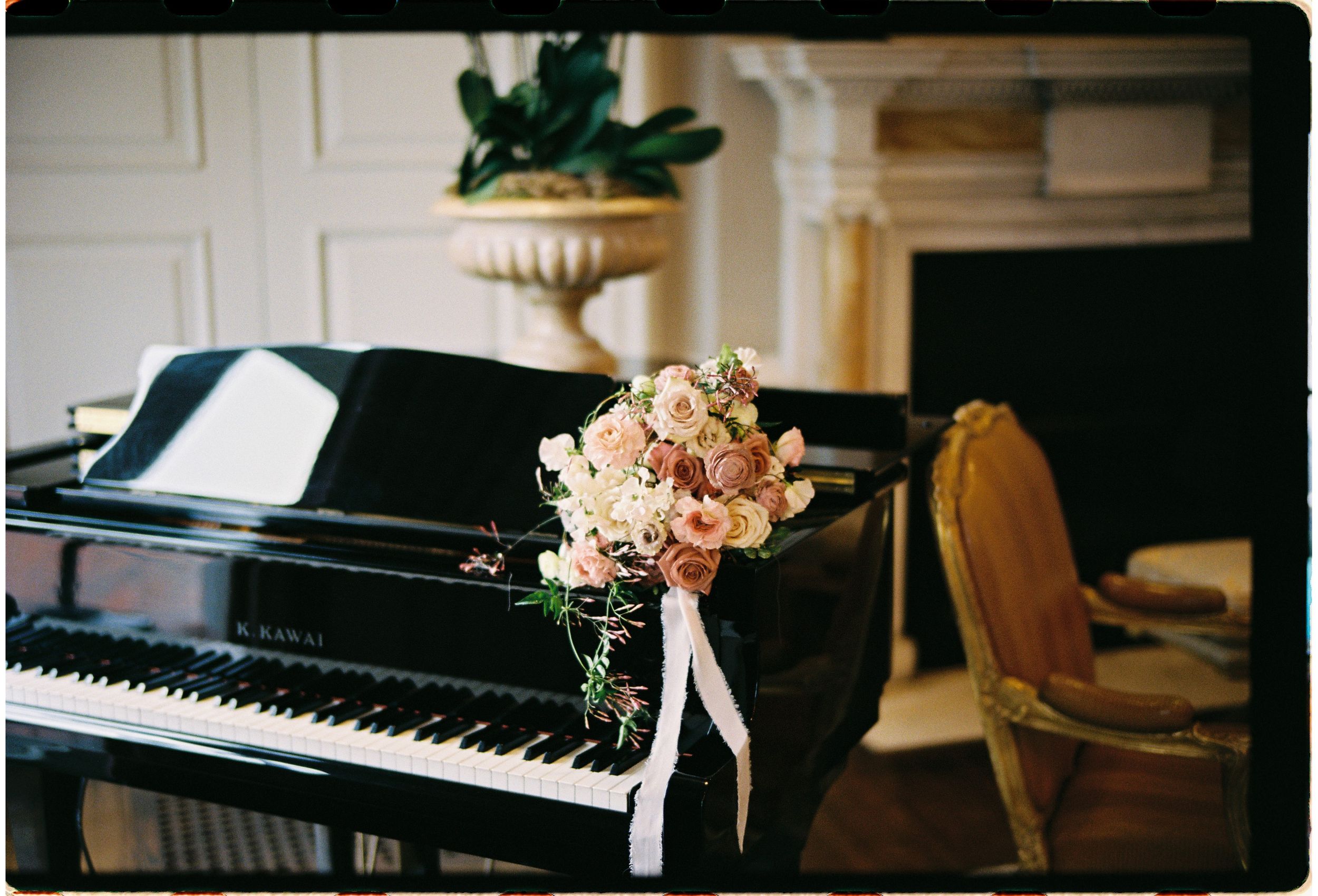 Vintage floral bouquet with pink roses sits atop a black grand piano in an elegant room with antique decor.