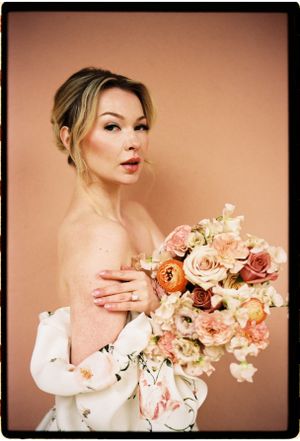 Elegant portrait with a stunning bouquet of peach and pink roses against a warm peach-colored backdrop.
