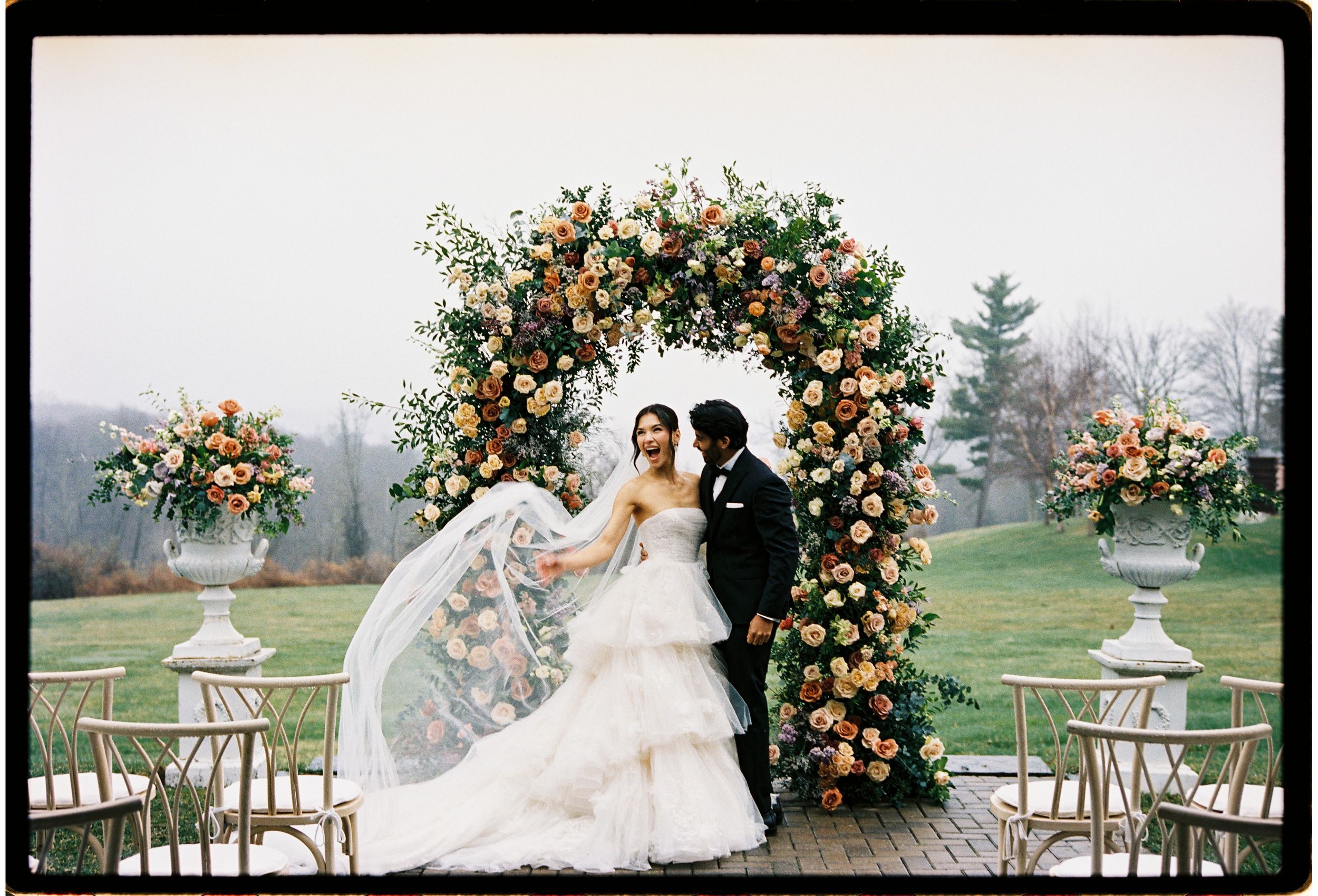 Beautiful outdoor wedding ceremony setup with floral arch and white chairs overlooking a misty countryside landscape.