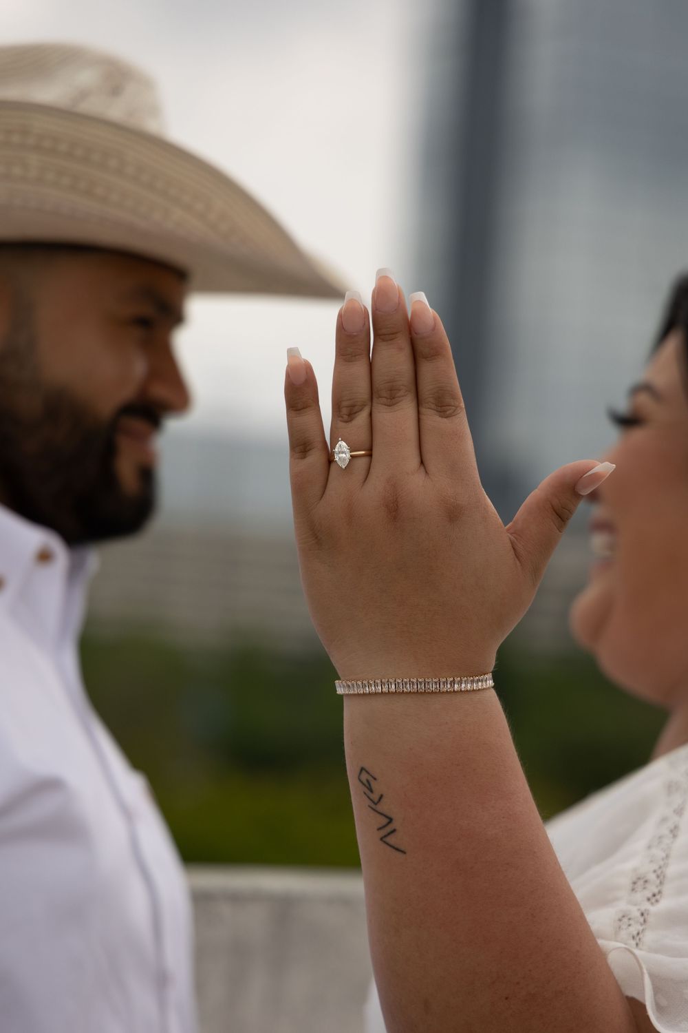 Close-up view of hands showing wedding rings against a blurred outdoor background.