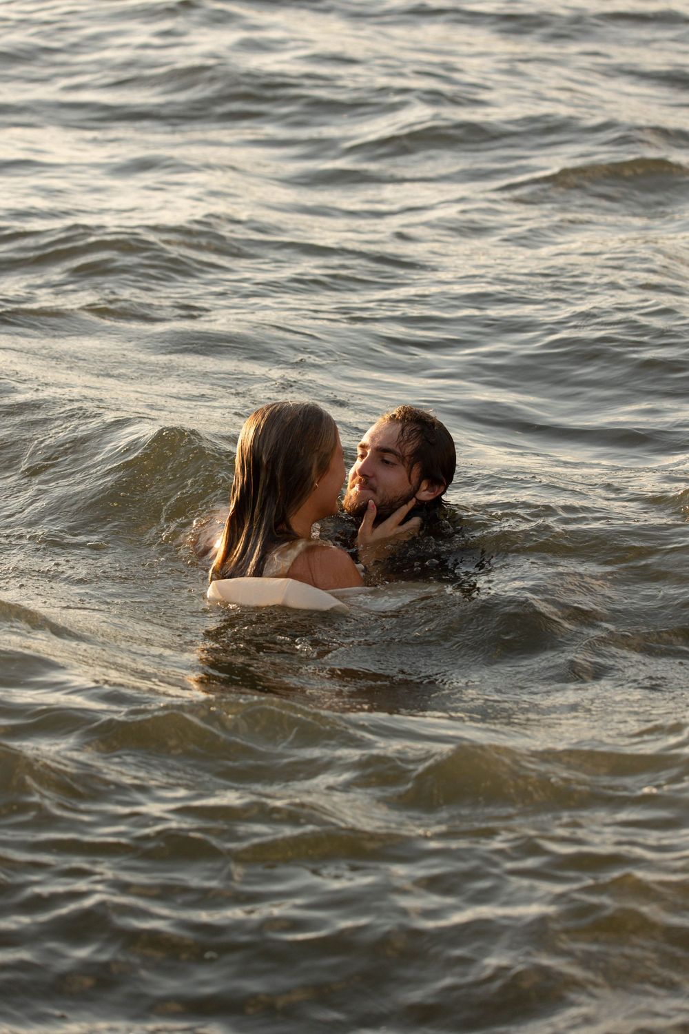Romantic couple sharing an intimate moment while swimming together in open water waves.