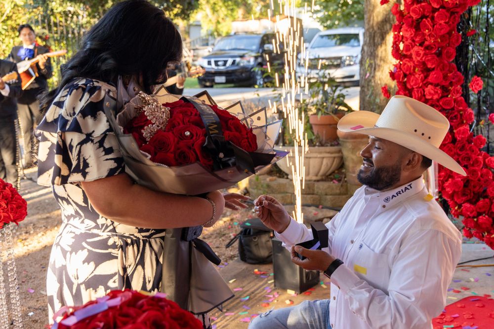 A heartfelt moment during a western-themed marriage proposal under a rose heart arch.