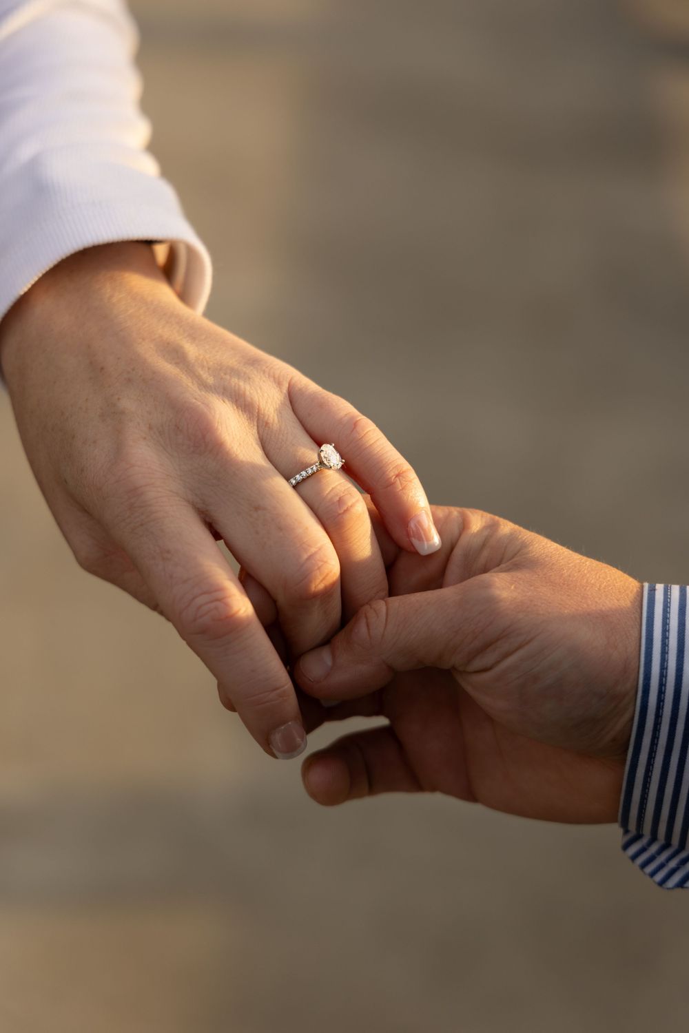 Close-up shot of hands with engagement ring in warm sunset light.