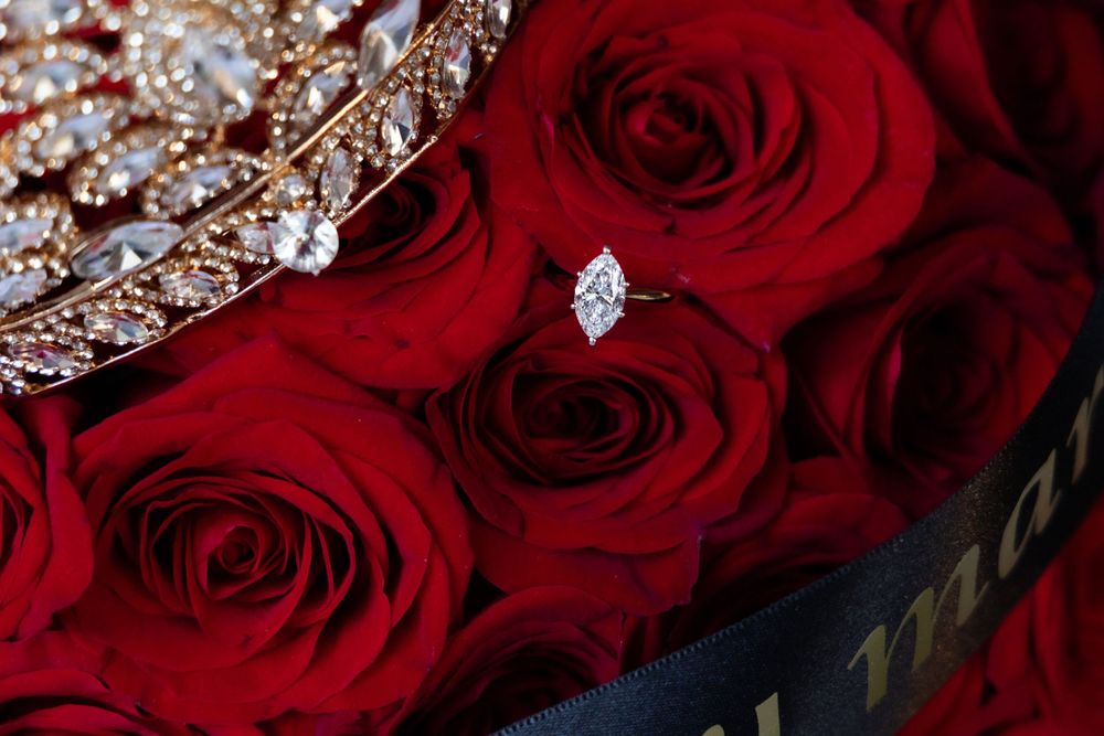 Close-up of diamond ring nestled among red roses with crystal crown detail.