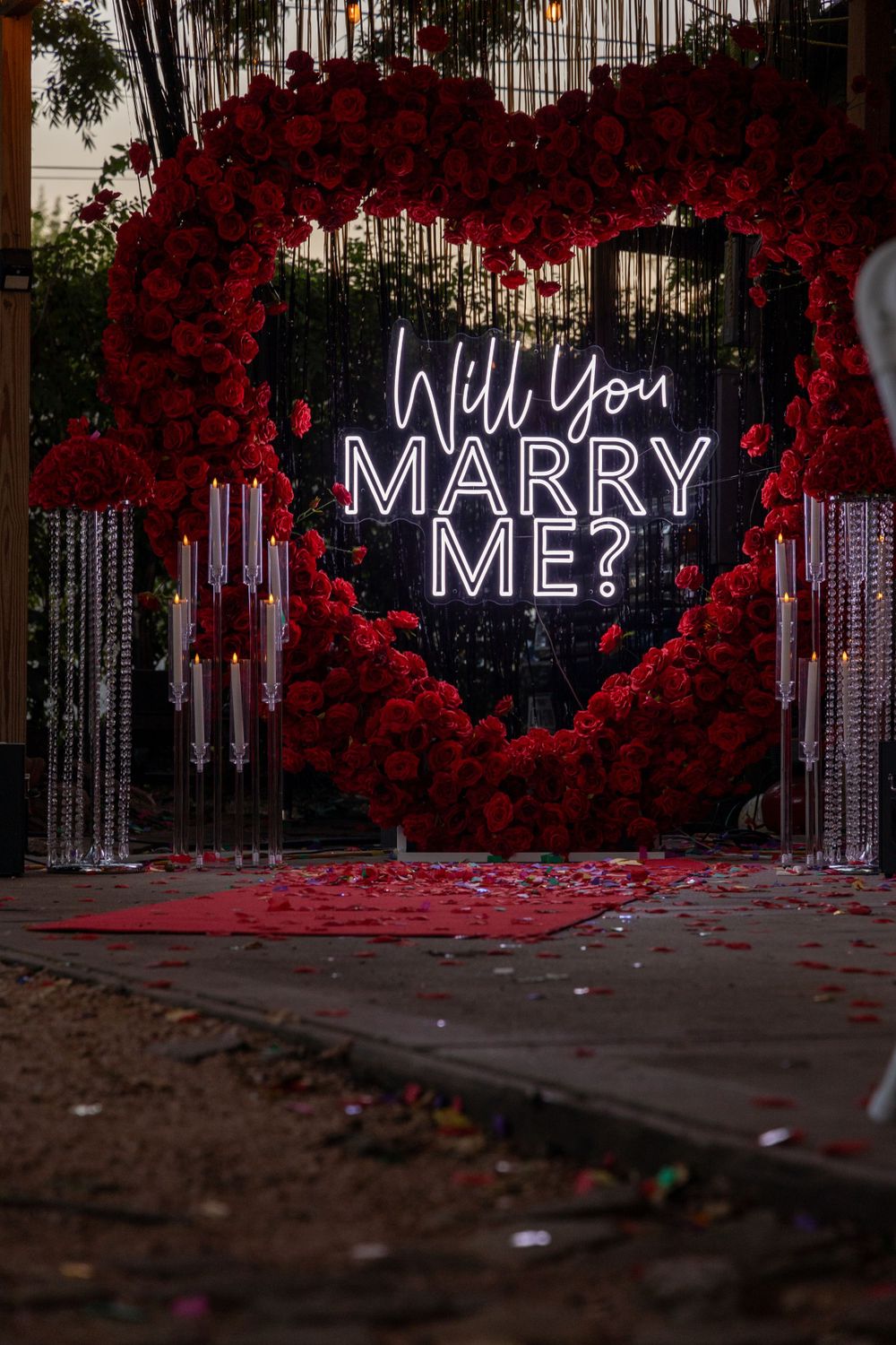 Romantic proposal display featuring heart-shaped red rose arch with neon signage.