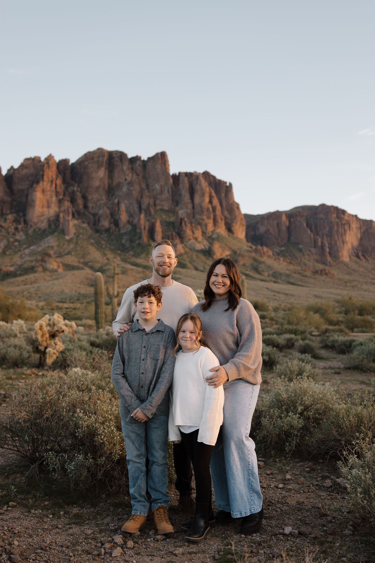 A family of four poses together against a backdrop of red desert cliffs and green trees.