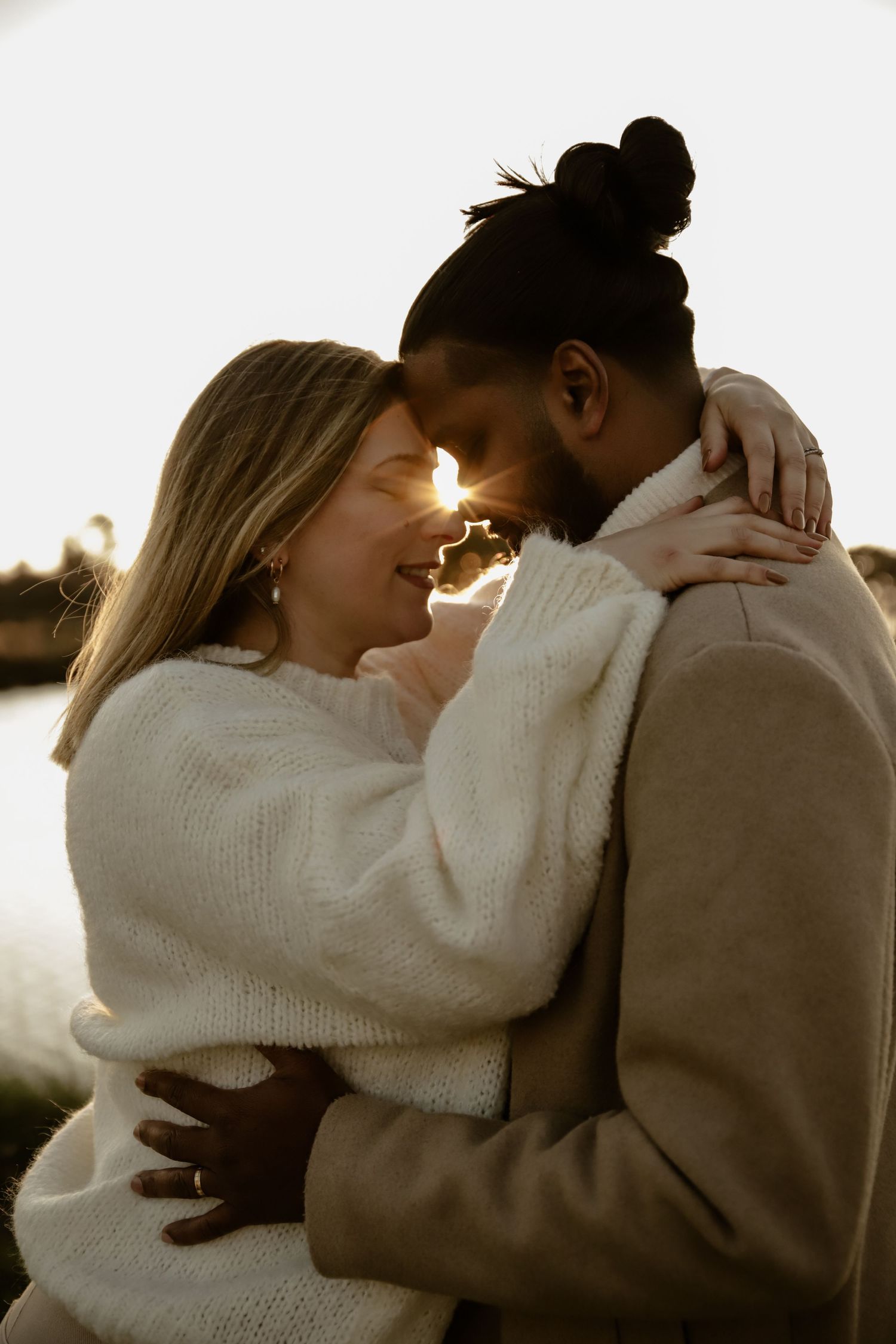 A couple in cozy sweaters shares an intimate embrace at sunset.