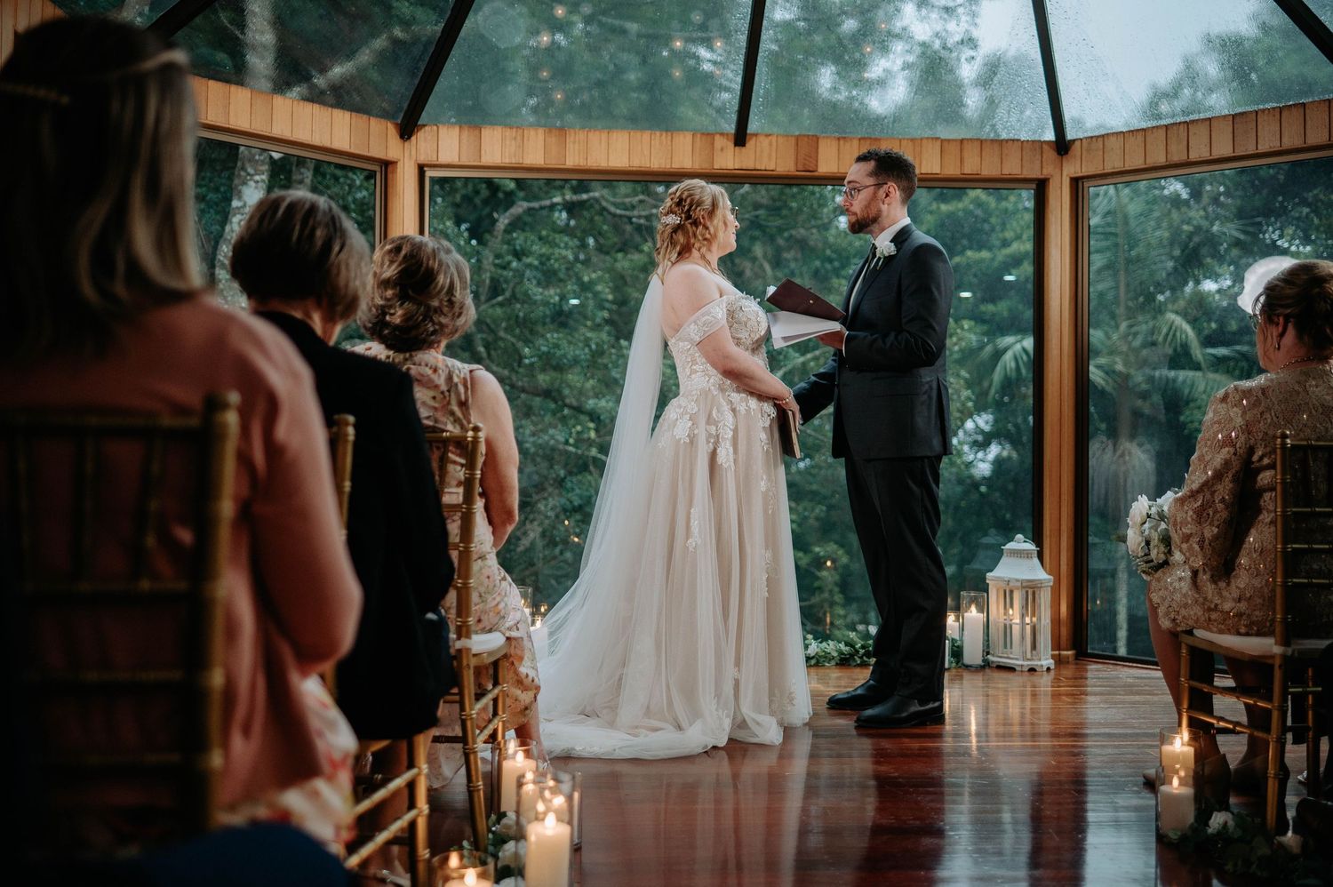 Romantic indoor wedding ceremony in rustic wooden pavilion with lantern-lined aisle.