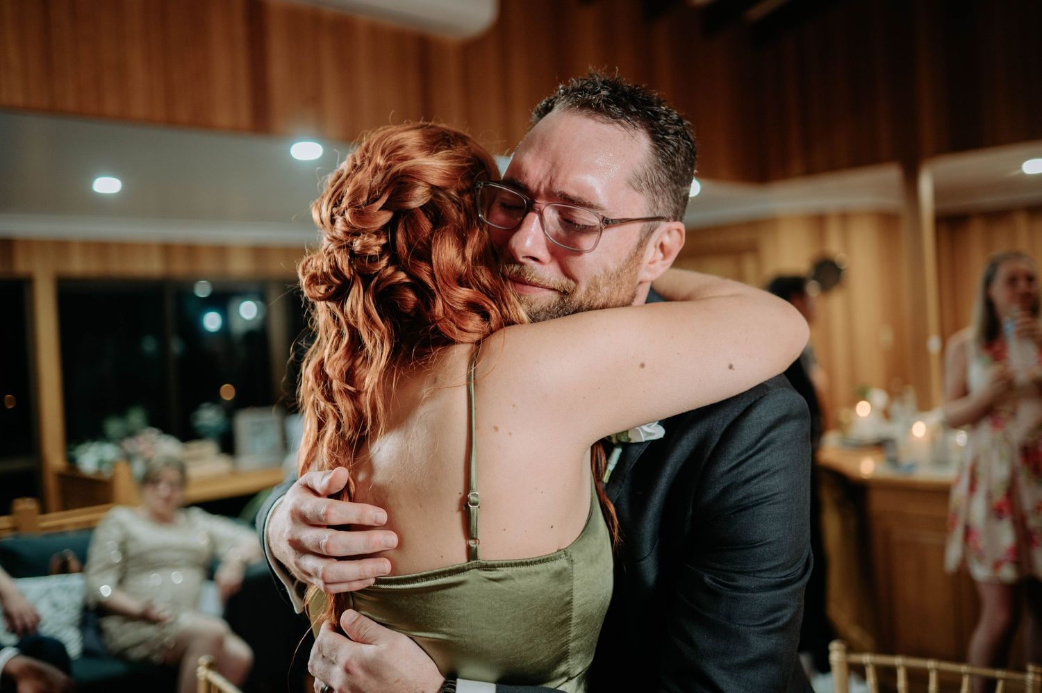 Emotional dance moment captured in wooden reception venue with warm lighting.