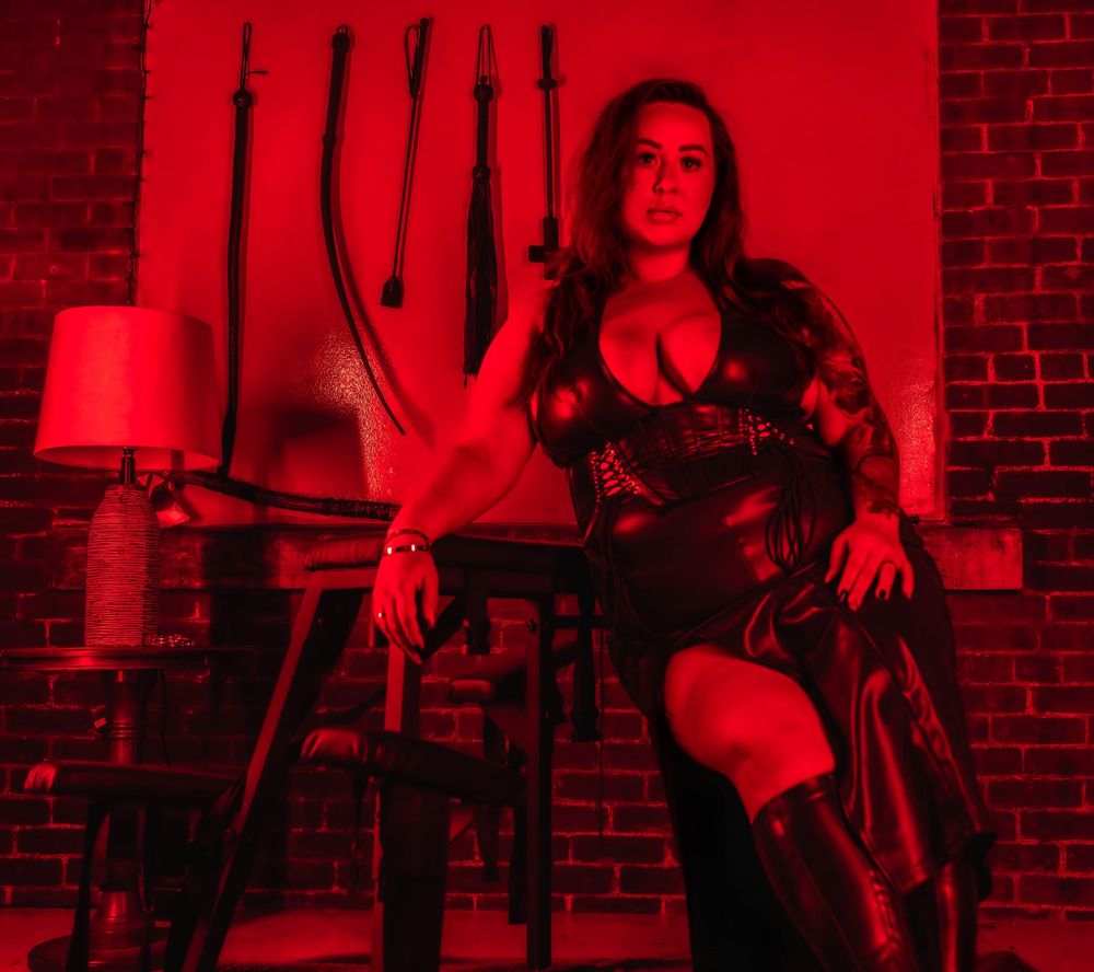 A person sits in a chair against a brick wall illuminated by dramatic red lighting in a moody atmosphere.