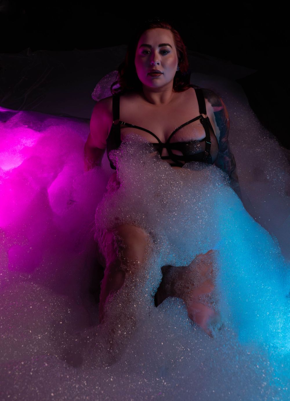 Artistic bathtub photography with dramatic pink and blue lighting creating a moody atmospheric scene.