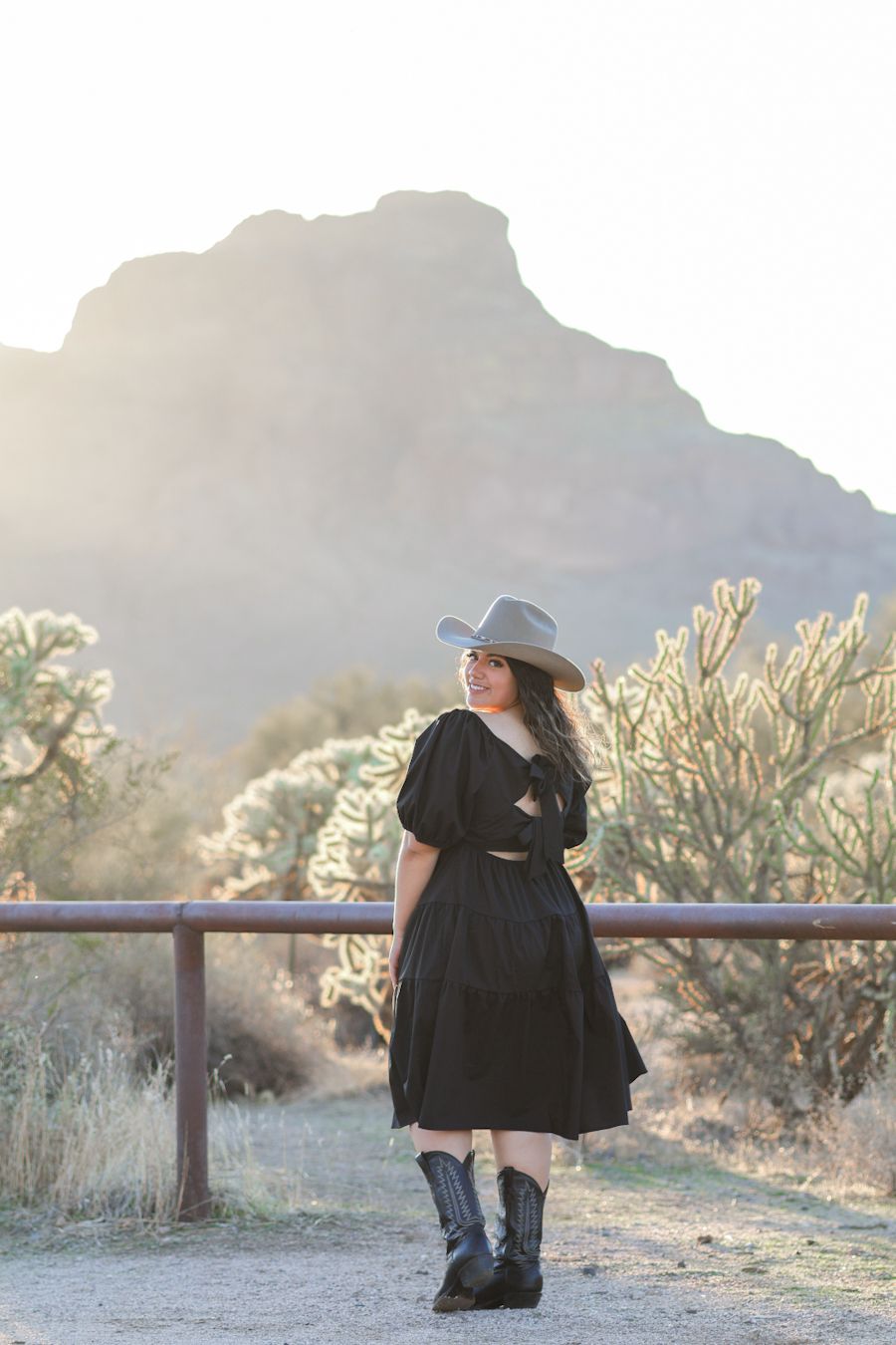 Light and airy senior portrait of a girl looking over her shoulder standing in front of a mountain near the Salt River in Mesa, Arizona.