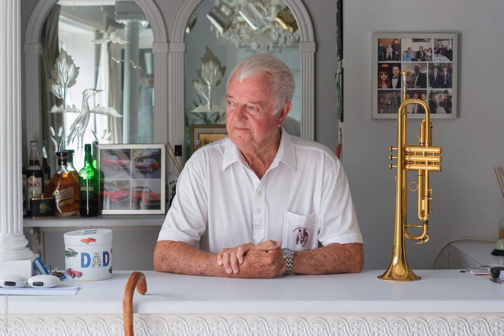 A person sits at a white counter with a decorative mirror and gold trumpet mounted on the wall in a home setting.