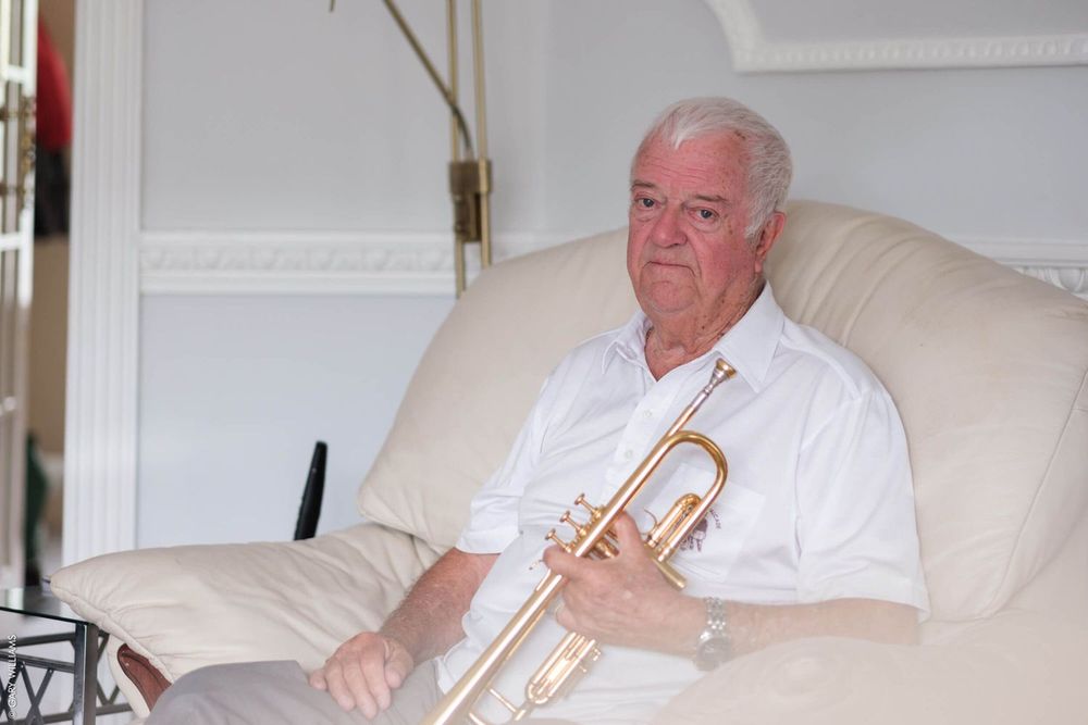 Musician in white shirt sits on light colored chair holding a brass trumpet.