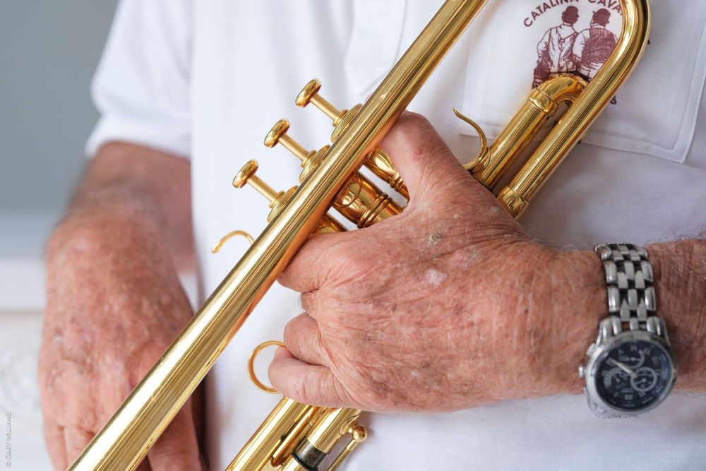 Close-up view of hands holding a brass trumpet while wearing a white shirt and silver watch.