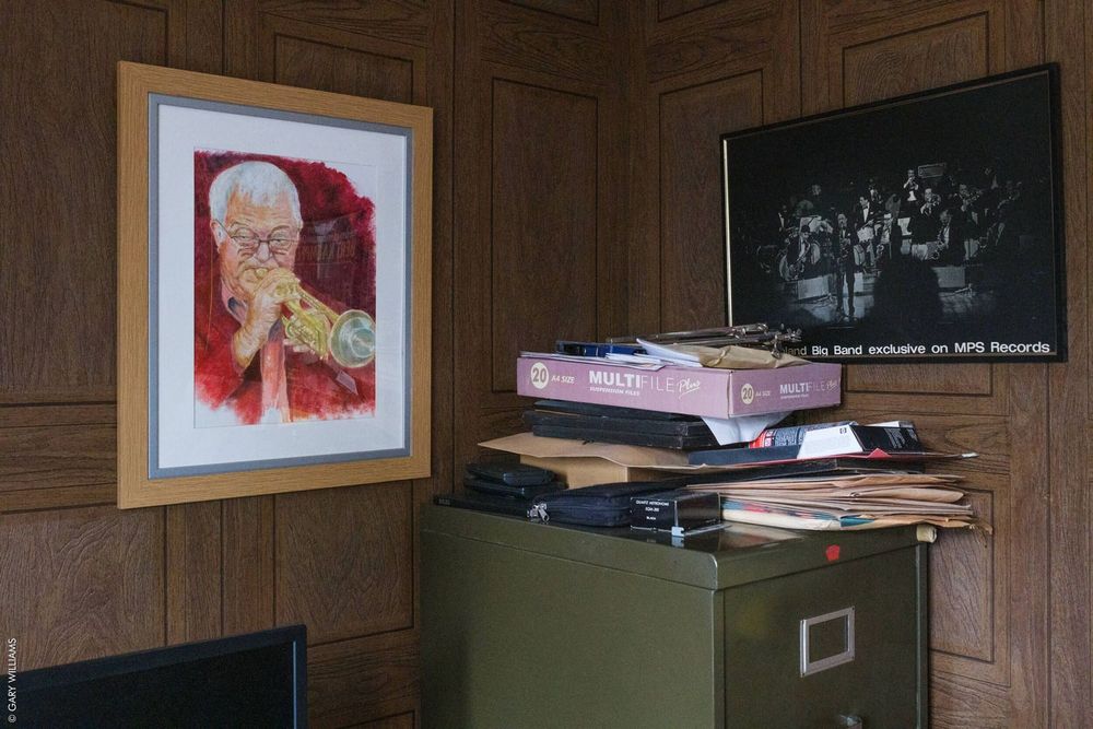 A filing cabinet against wood paneled walls with framed artwork and photographs displayed above.