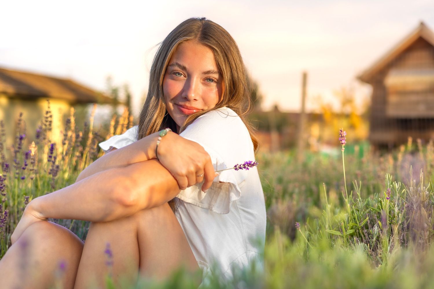 A person wearing white sits in a golden-lit wildflower meadow at sunset with lavender blooms in the foreground.